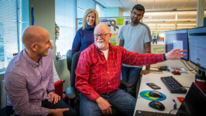 Four Microsoft employees on the Network Automation Delivery Team talk and laugh as Steve Kern gestures to his monitor.